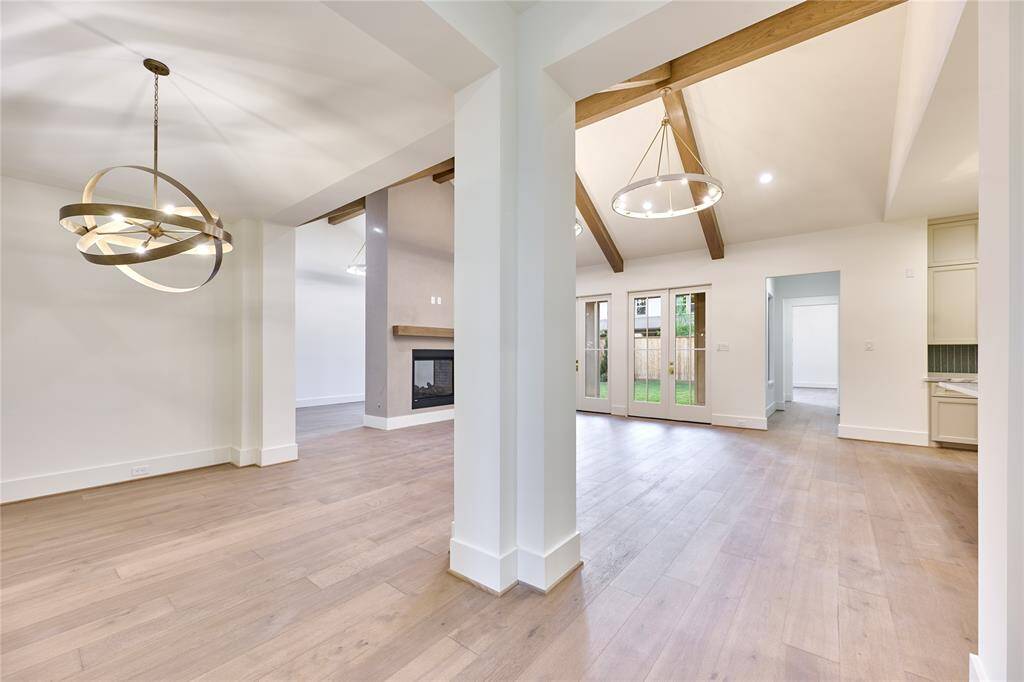 This photo showcases a spacious open-concept living area with elegant light fixtures, large windows, and exposed wooden beams. The room features engineered white oak floors and a modern fireplace, creating a warm and inviting atmosphere.