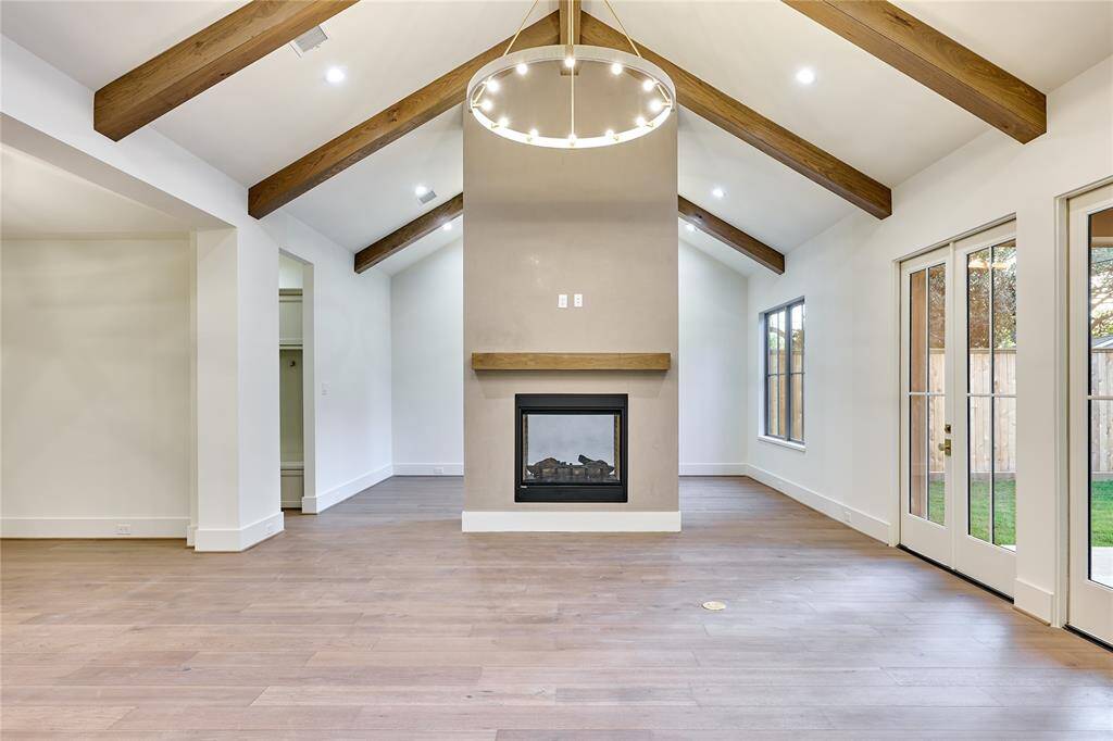 This spacious living area features vaulted ceilings with wooden beams, a modern fireplace, and French doors that open to a backyard. Perfect for cozy and bright living.