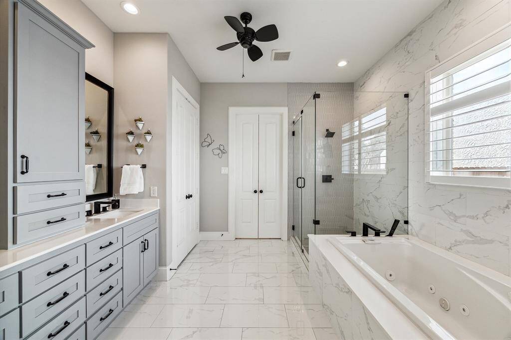 Luxurios primary bath with sleek white tile flooring, 5-foot jetted soaker tub and walk-in shower with glass enclosure.