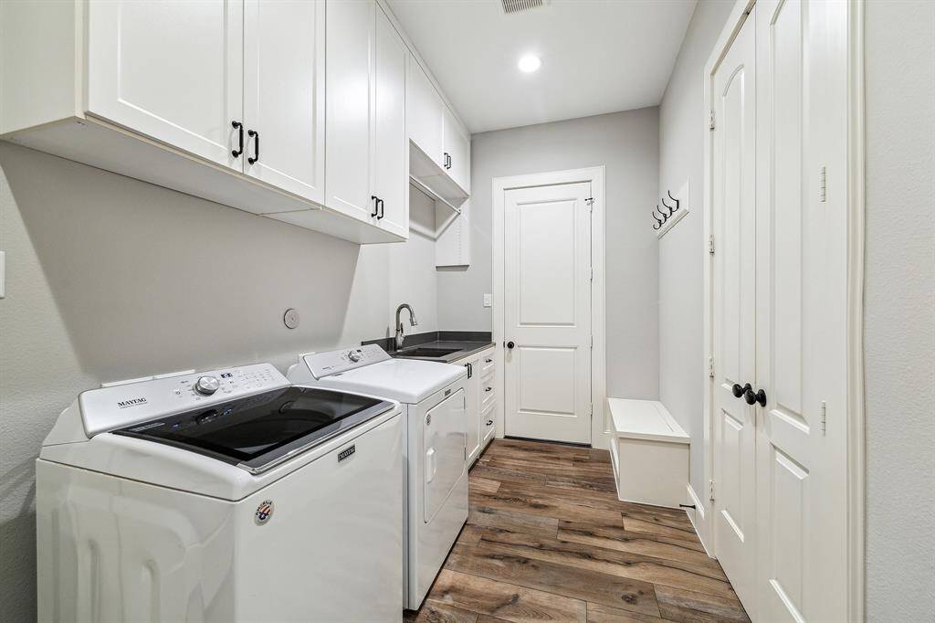 The spacious laundry room features ample storage, a sink, a stainless steel clothing rod, and a seating bench. It includes a back door leading to the outside and a door to the garage.
