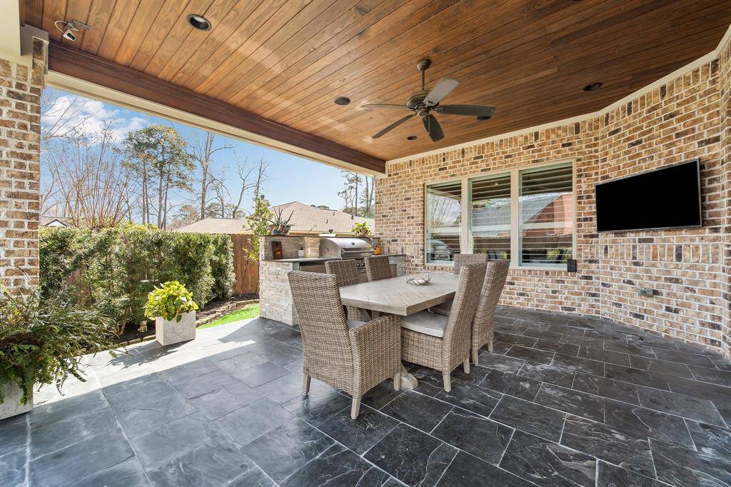 The covered patio features slate flooring, a tongue-and-groove stained oak ceiling, a ceiling fan, and a built-in soundbar system.