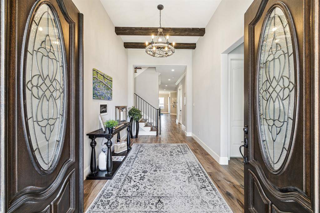 Elegant entryway featuring double French doors with intricate detailing. The foyer boasts high ceilings with wxposed wood beas and a statement chandelier.