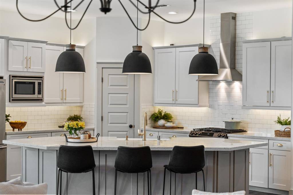 Three custom dark grey pendant lights with modern silhouettes anchor the island, their rich charcoal finish complement the home’s neutral palette while adding a striking contrast.