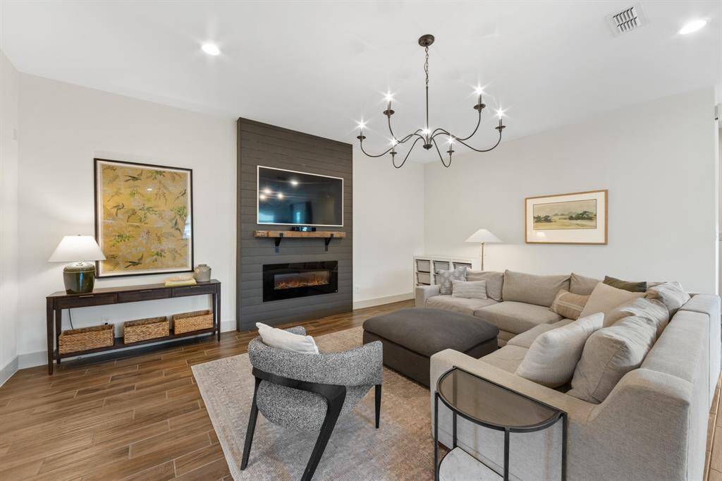 The family room's floor-to-ceiling dark grey brick chimney wall harmonizes with the kitchen’s trio of dark grey pendant lights, creating a cohesive modern-industrial aesthetic.