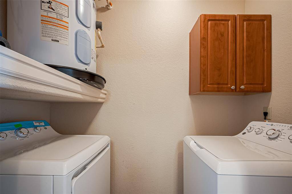 Enjoy the laundry room featuring a washer and dryer set, a wall-mounted water heater, and a wooden storage cabinet.
