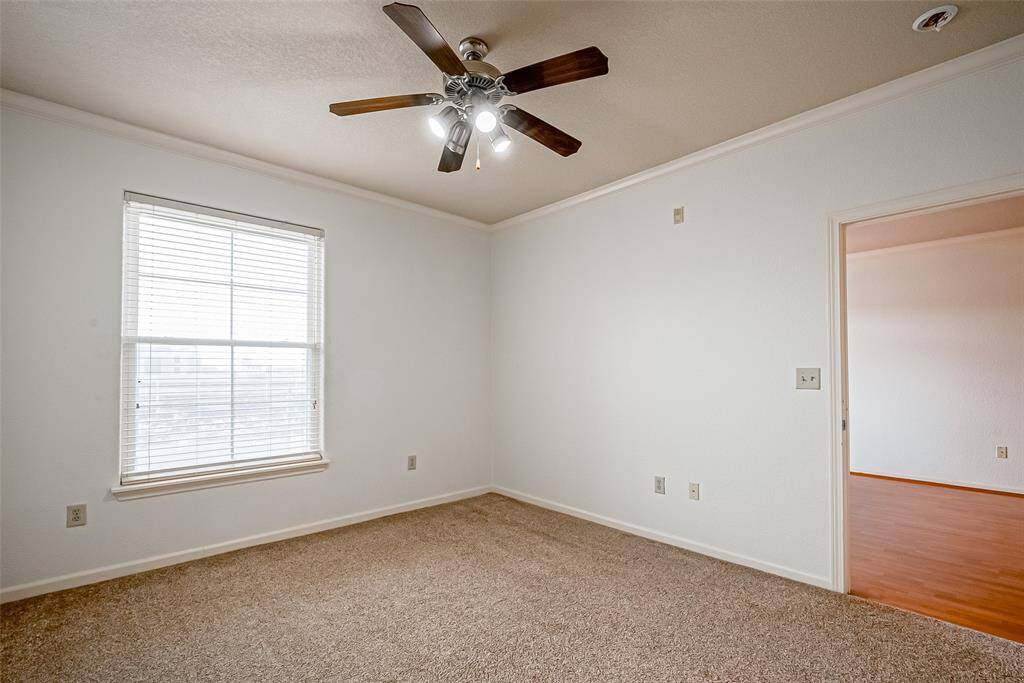 This room is bright and inviting with neutral walls and carpet. It features a ceiling fan and a large window, offering ample natural light. The adjoining space has laminate flooring, adding warmth and contrast.