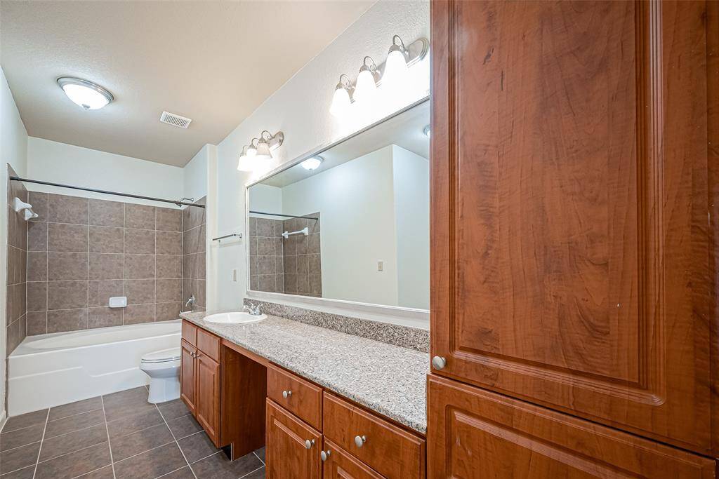 This bathroom features a spacious layout with a large vanity and granite countertop, ample cabinetry, and a tiled shower-tub combo.
