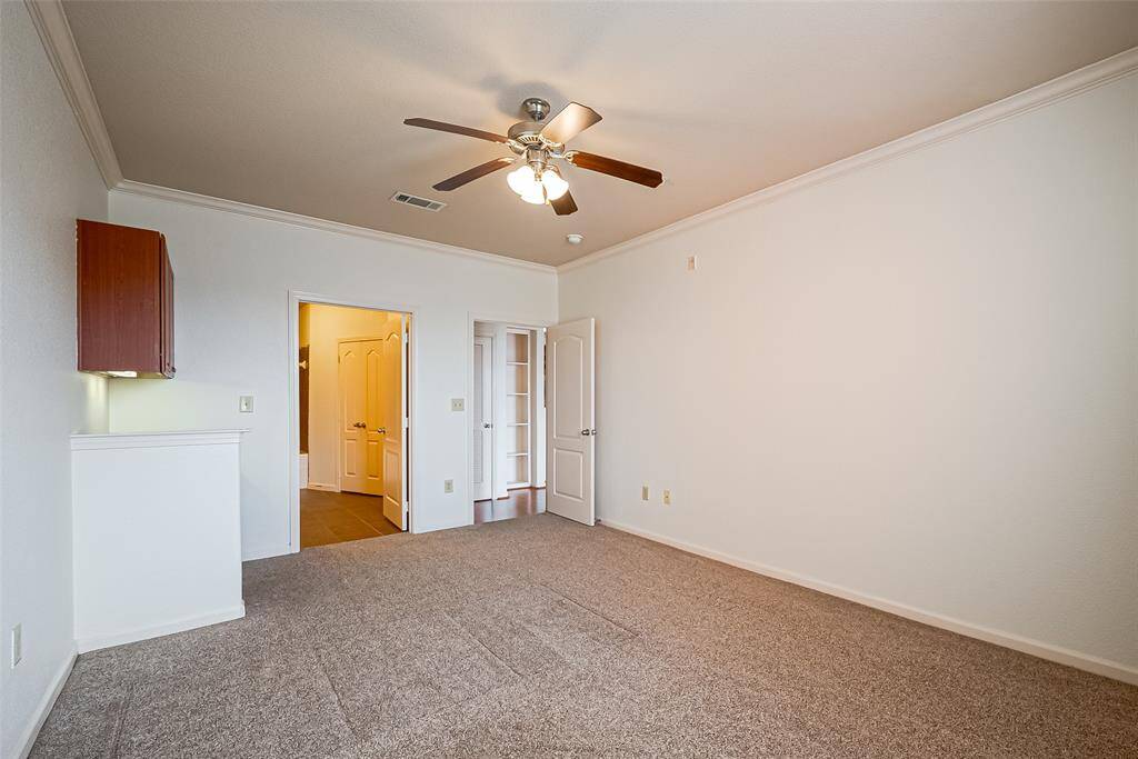 This bedroom features neutral carpeting, a ceiling fan with lights, and study desk.