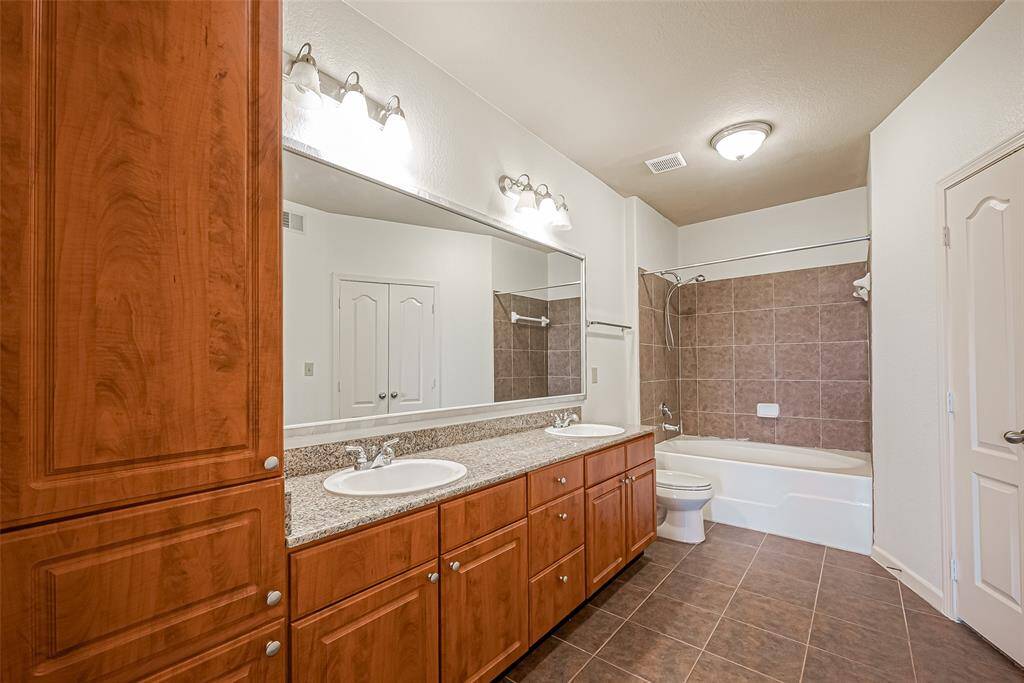 This bathroom features dual sinks with granite countertops, elegant wooden cabinetry, and a full-sized bathtub with a tiled surround.