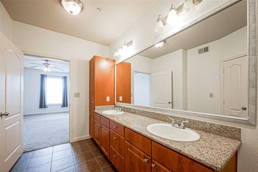 Spacious bathroom with a large dual-sink vanity featuring granite countertops and ample wooden cabinetry.