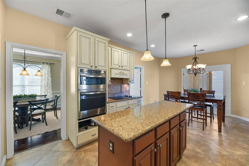 The kitchen transitions into a comfortable and cozy eat-in breakfast room with a space for a table beneath the scrolled iron chandelier. Also note the diagonally laid tile floors, adjacent utility room, and French doors leading out to the backyard pool area.