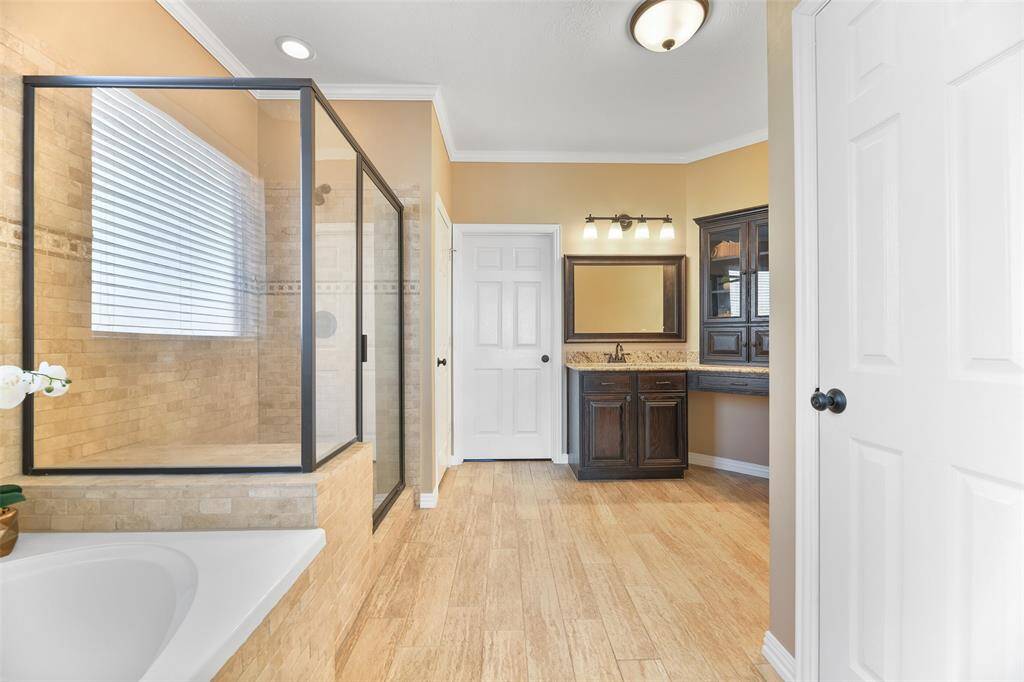 Step into the updated master bathroom and note the wrap-around vanity with granite countertops, separate his & hers undermount sinks, beautifully stained woodwork, wood-look tile floors, a soaking tub, and an oversized glass enclosed shower with a bench seat & a travertine tile surround.