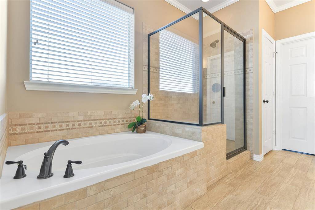 Step into the updated master bathroom and note the wrap-around vanity with granite countertops, separate his & hers undermount sinks, beautifully stained woodwork, wood-look tile floors, a soaking tub, and an oversized glass enclosed shower with a bench seat & a travertine tile surround.
