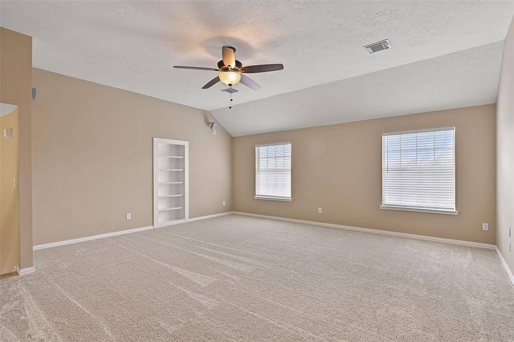 Atop the sweeping staircase from the foyer is this extra spacious game room with an elevated gambrel ceiling, a lighted ceiling fan, wired speakers, rear-facing windows, and a built-in bookshelf that opens to reveal a hidden storage space.