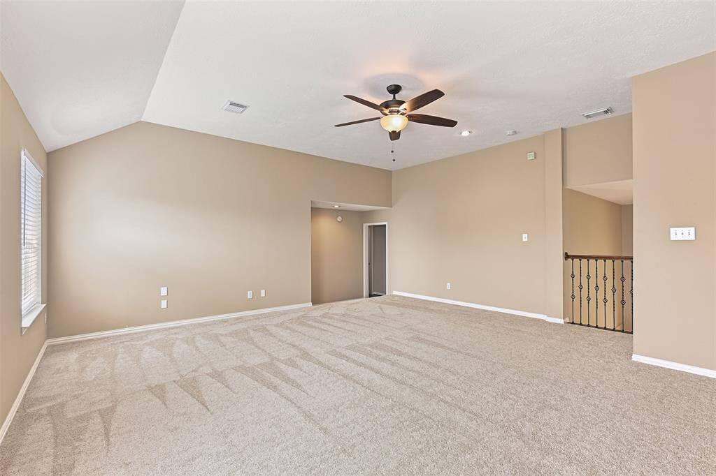 Atop the sweeping staircase from the foyer is this extra spacious game room with an elevated gambrel ceiling, a lighted ceiling fan, wired speakers, rear-facing windows, and a built-in bookshelf that opens to reveal a hidden storage space.