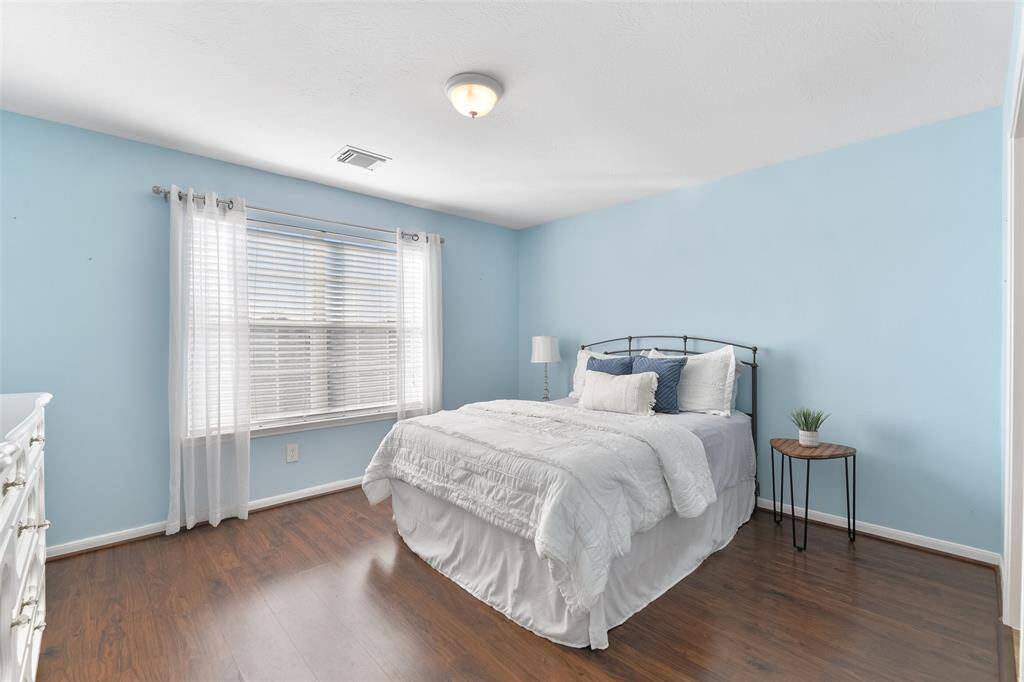 The first of three secondary bedrooms that are located on the second floor offers a custom sky-blue paint selection, wood-look laminate floors, an expansive window shaded by 2-inch blinds, a walk-in closet, and a shared Jack & Jill style bathroom.