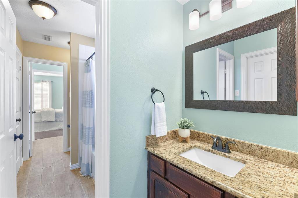 This Jack & Jill style bathroom services the upstairs bedrooms and it offers dual sinks, a granite top vanity, stained wood cabinetry, a framed mirror, stylish lighting, wood-look tile floors, and a combination bathtub and shower with a classic white tile surround.