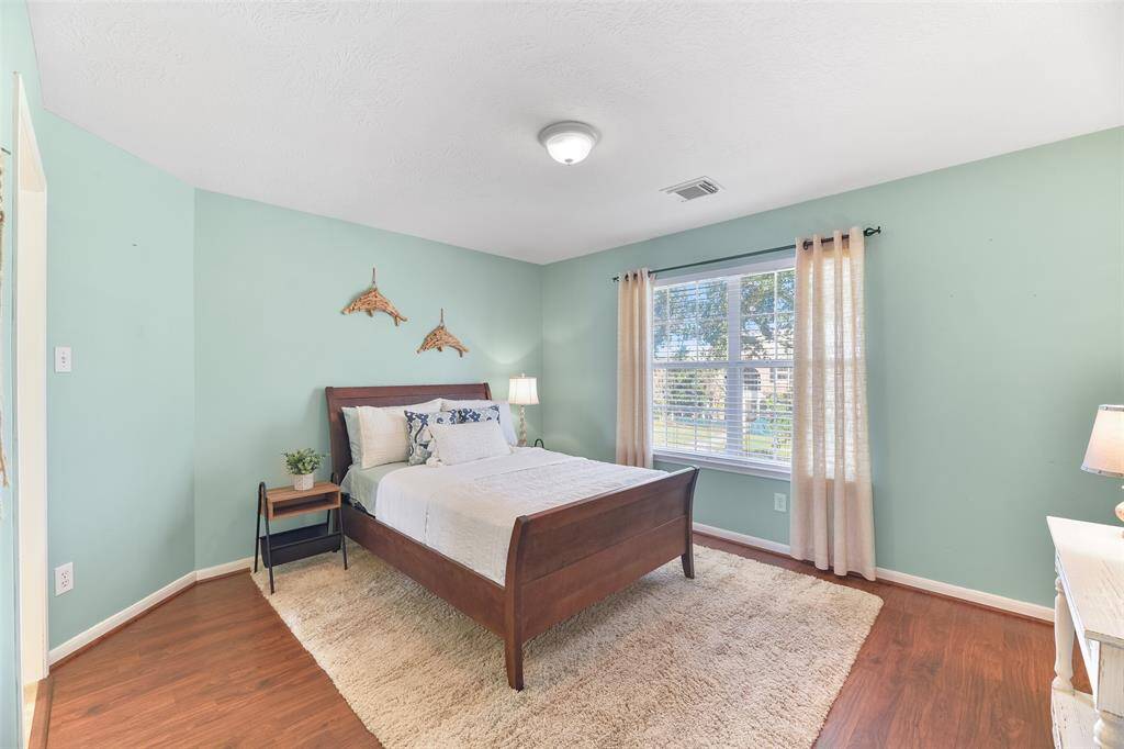 Another upstairs bedroom features a peaceful aquamarine blue paint, wood-look laminate floors, a front-facing window dressed with 2-inch blinds and linen draperies, a walk-in closet, and a shared Jack & Jill style bathroom.