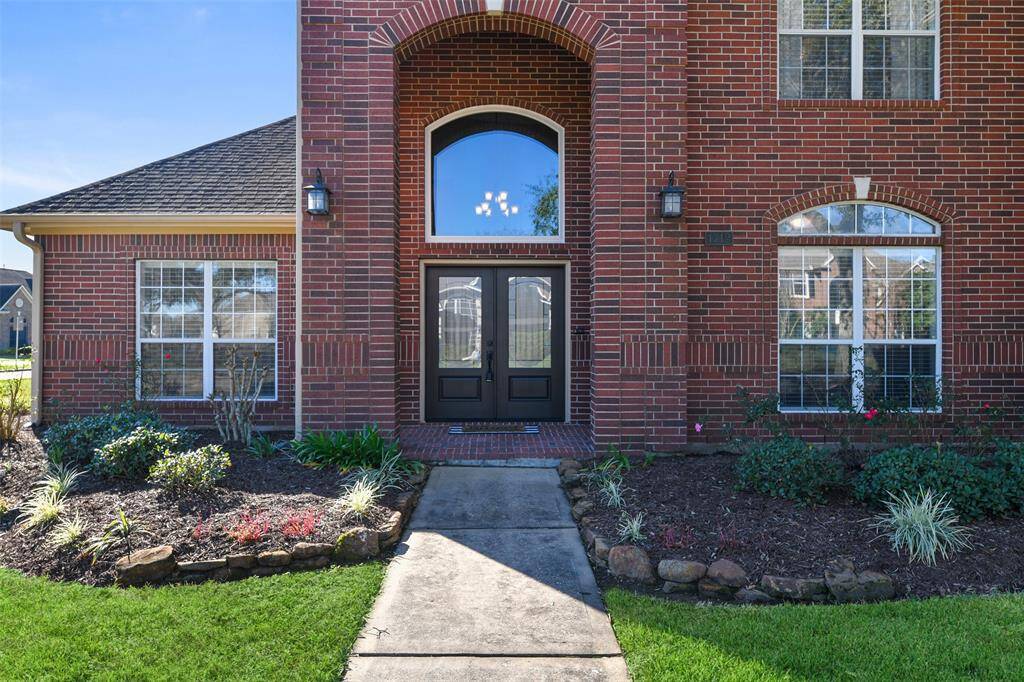 A concrete path leads from the street up between the rock-lined landscape beds with in-ground sprinklers to a covered front porch and a newly updated grand double-door entry topped by an undivided palladium arched window.