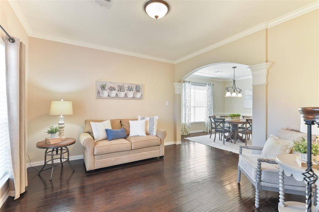 On the left side of the foyer, a wide arched entrance leads into a formal living space with an adjoining formal dining space. Note the fresh neutral paint, crisp white crown molding, engineered wood floors, and a front-facing window shaded by 2-inch blinds.