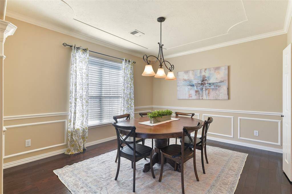 Gather for a meal in this formal dining room that features a scrolled iron pendant light, elegant crown, chair rail, and picture frame moldings, engineered wood floors, a side-facing window with 2-inch blinds, and convenient direct access to the kitchen.