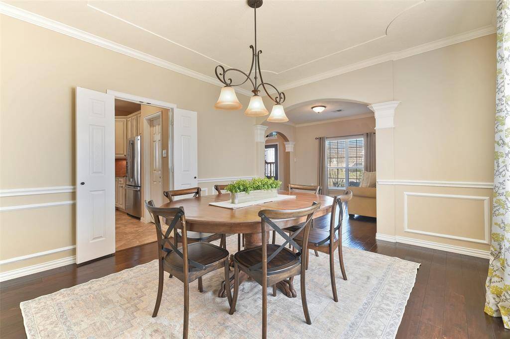 Gather for a meal in this formal dining room that features a scrolled iron pendant light, elegant crown, chair rail, and picture frame moldings, engineered wood floors, a side-facing window with 2-inch blinds, and convenient direct access to the kitchen.