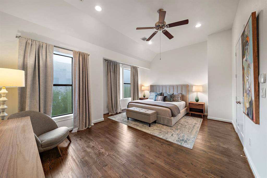 Tall ceilings and dual windows bring beautiful natural light into the primary suite, with rich hardwood floors creating a grounded, serene setting for rest and relaxation.