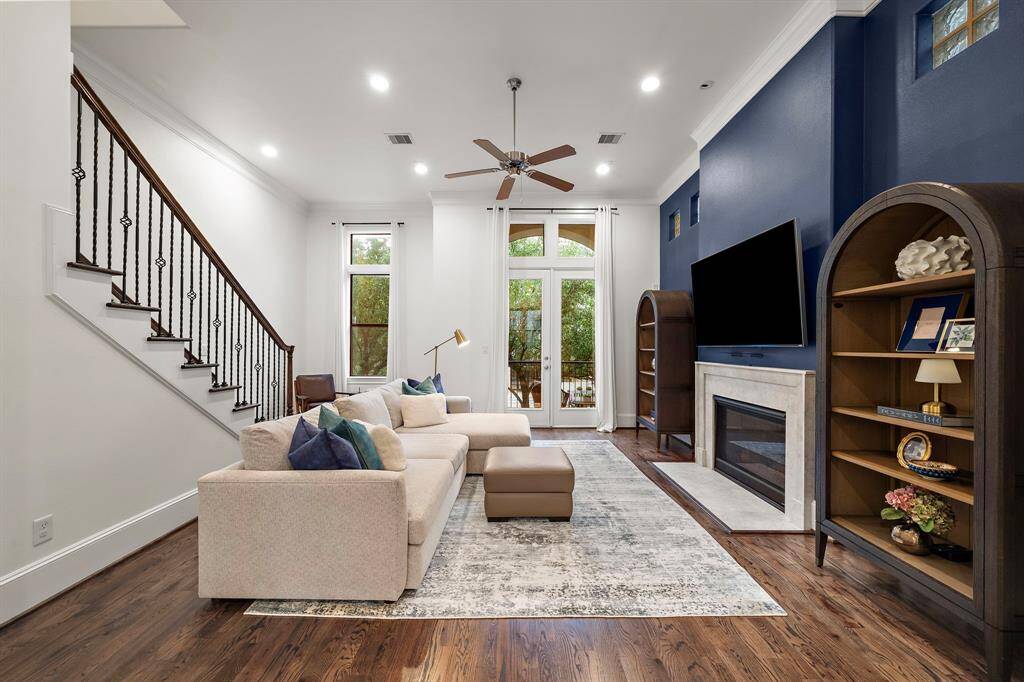 Soaring ceilings and wall-to-wall natural light elevate the living room’s sense of space, while hardwood floors and a fireplace lend warmth and character. French doors open to the front patio, blending indoor comfort with inviting outdoor flow.