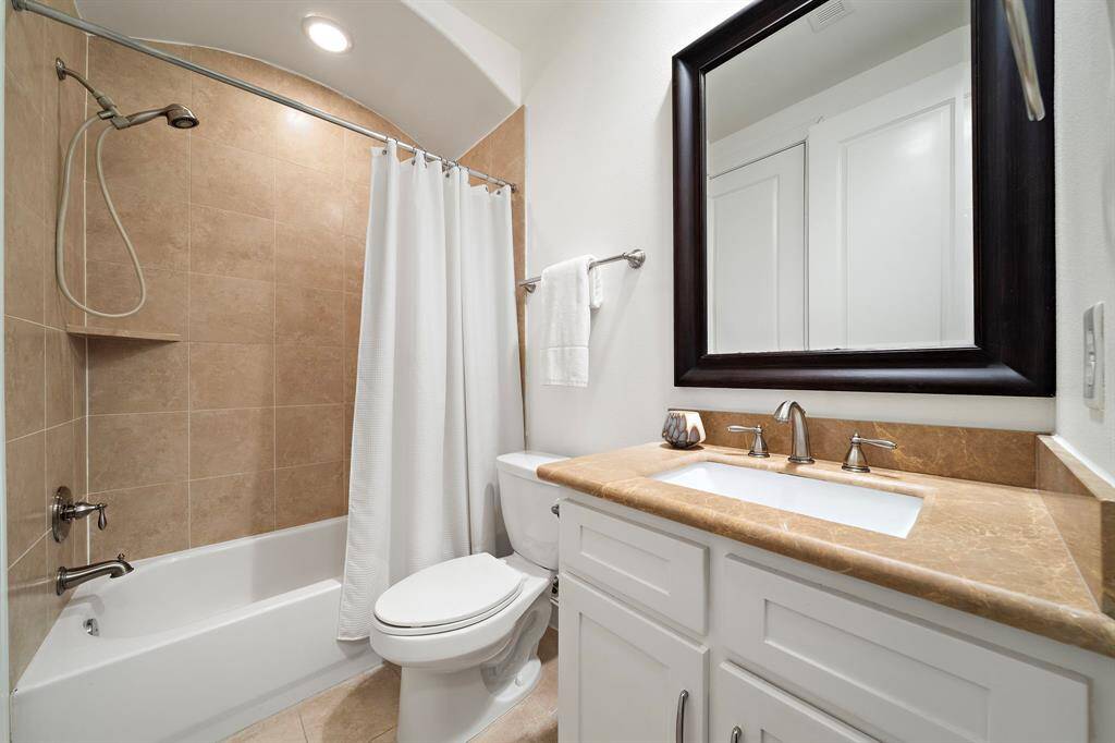 This private ensuite bath features a full tub/shower combo with neutral tile surround, a wide vanity with generous counter space, and classic finishes that complement the home’s overall design.