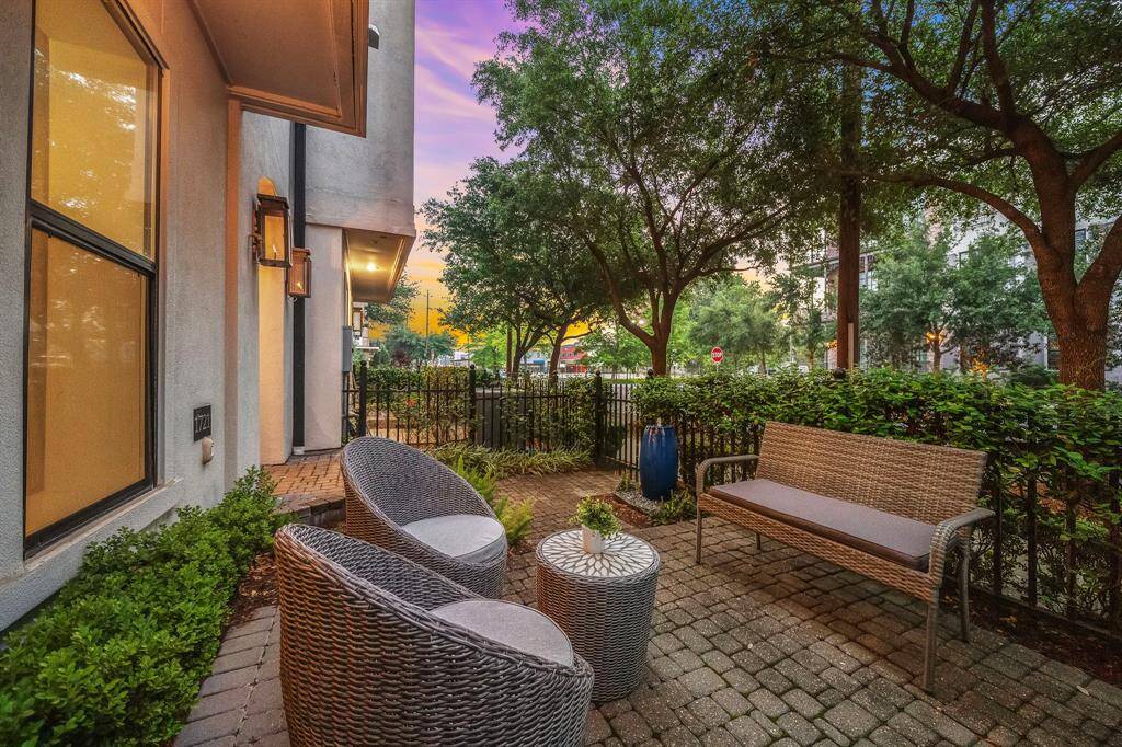 The gated front patio offers a charming space to unwind beneath a canopy of mature trees, with a paver stone surface and seating area framed by neatly trimmed greenery. Thanks to the thoughtful orientation, it doesn’t look directly into neighboring homes—providing enhanced visual privacy that’s rare in townhome living.