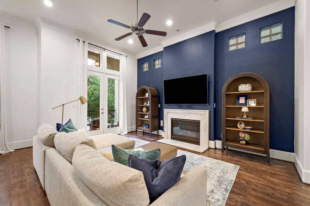 Tall windows and French doors invite natural light into the living space, where rich wood floors and custom navy accents frame a welcoming atmosphere for everyday lounging or casual gatherings.
