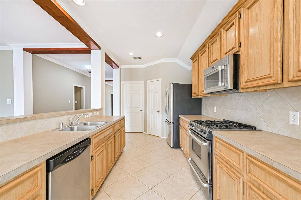 This kitchen features a spacious layout with tile flooring, wooden cabinetry, and stainless steel appliances. It opens into a living area with a cozy fireplace, creating a warm and inviting space.