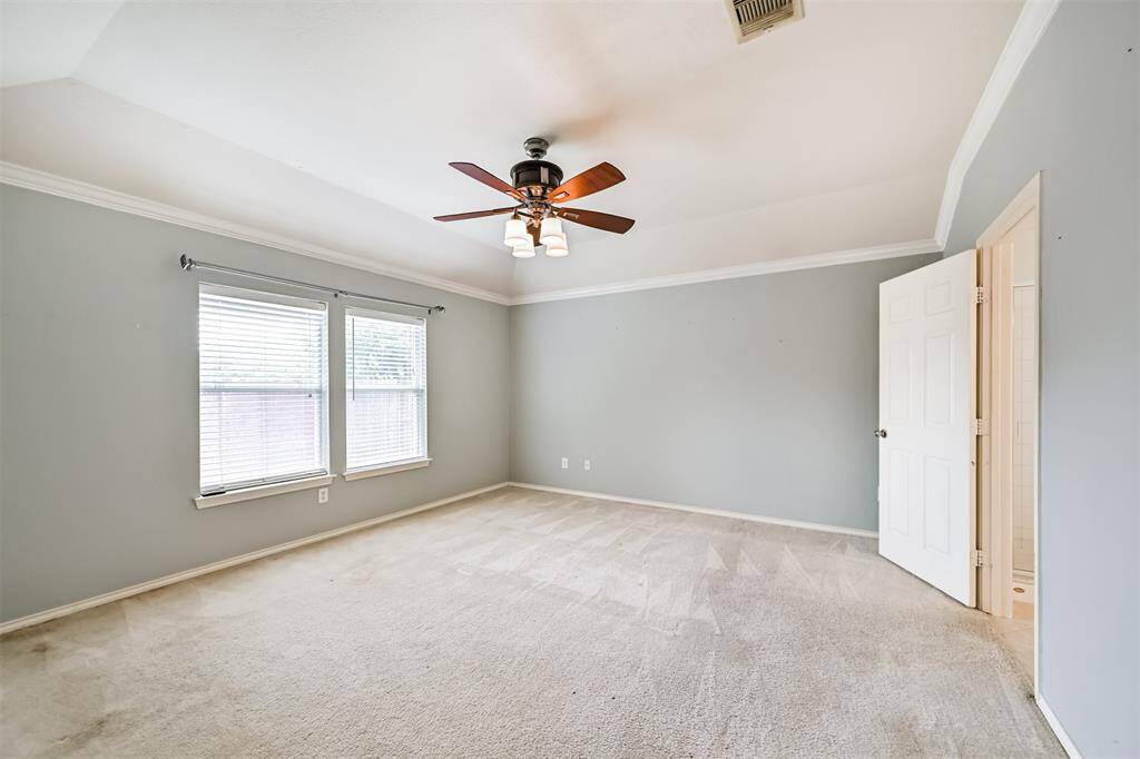Spacious primary bedroom with neutral walls, crown molding, and a ceiling fan. It features an open doorway leading to a bathroom and a closet. The room receives ample natural light, creating a bright and inviting atmosphere.