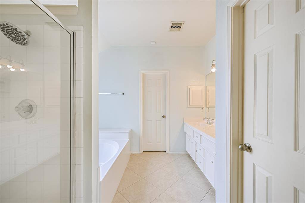 A spacious bright Primary bathroom  features a glass-enclosed shower, a separate bathtub, and a double sink vanity with ample storage. Separate WC.