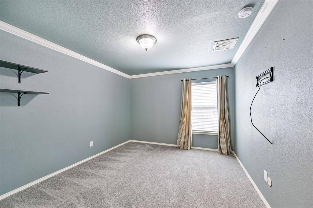 This room features soft blue walls with white trim, a single window with light curtains, wall-mounted shelves, and a carpeted floor. There's a light fixture on the ceiling and a mount for a TV on the wall.