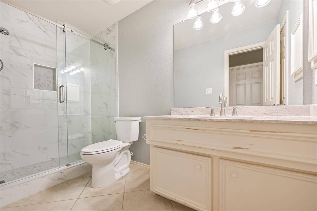 The guest bathroom features a newly updated modern design with a glass-enclosed shower, marble-style tiles, a spacious vanity and elegant lighting.