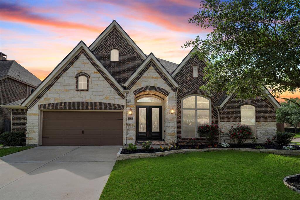 This sprawling single-story Perry home stuns at sunset, showcasing elegant brick and stonework, a stately double-door entry, and pristine landscaping on a premium corner lot.