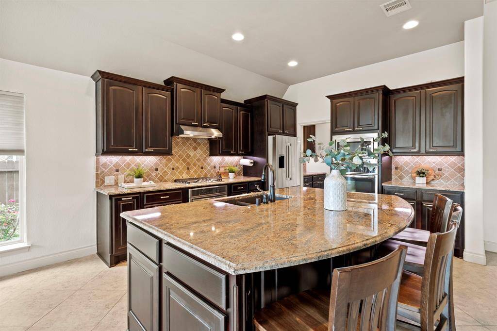 This fully loaded kitchen features rich espresso cabinetry, granite countertops, a coordinating backsplash, and stainless steel appliances, including a gas cooktop and double ovens.