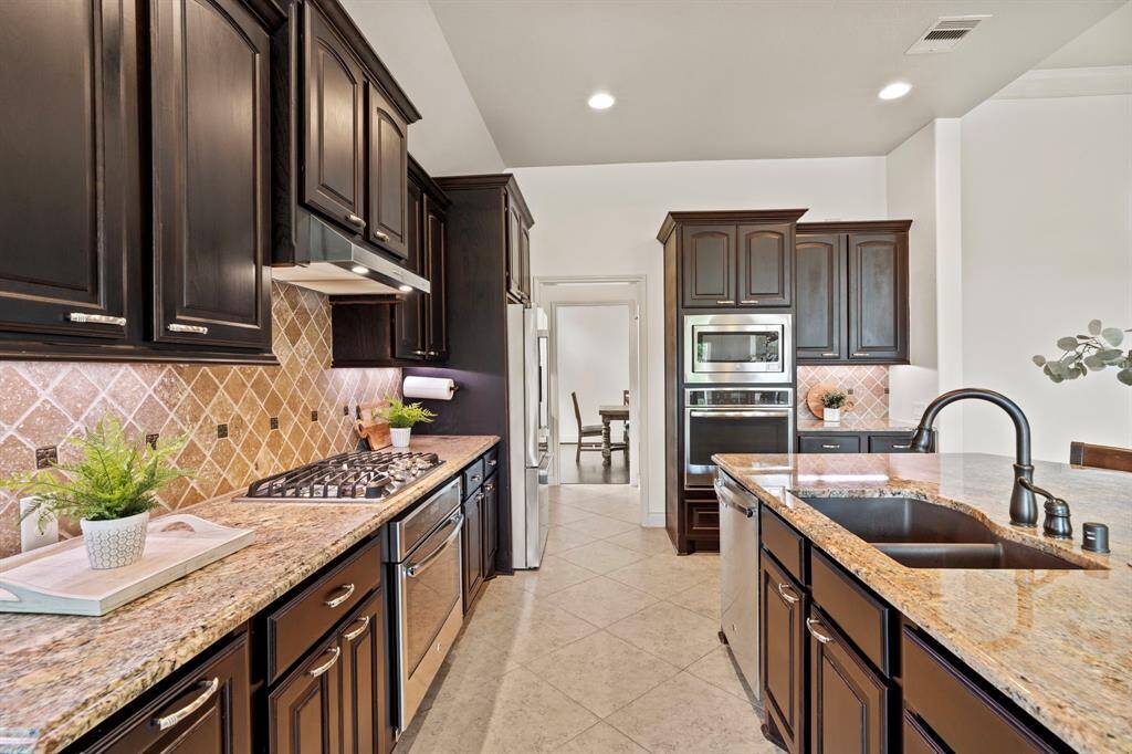 A closer look at the cooking zone reveals ample counter space, upper and lower cabinetry, and stylish tile backsplash that ties the design together beautifully.