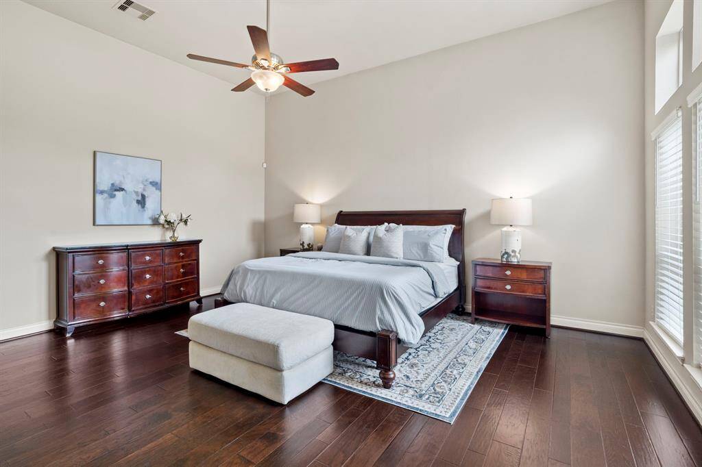 The serene primary bedroom offers rich wood flooring, a soaring ceiling with a cooling fan, and ample space for a king-sized bed and more.