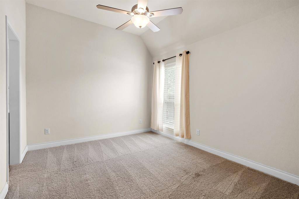 This spacious third bedroom features soft carpet, high ceilings, and a large window that fills the room with natural light.