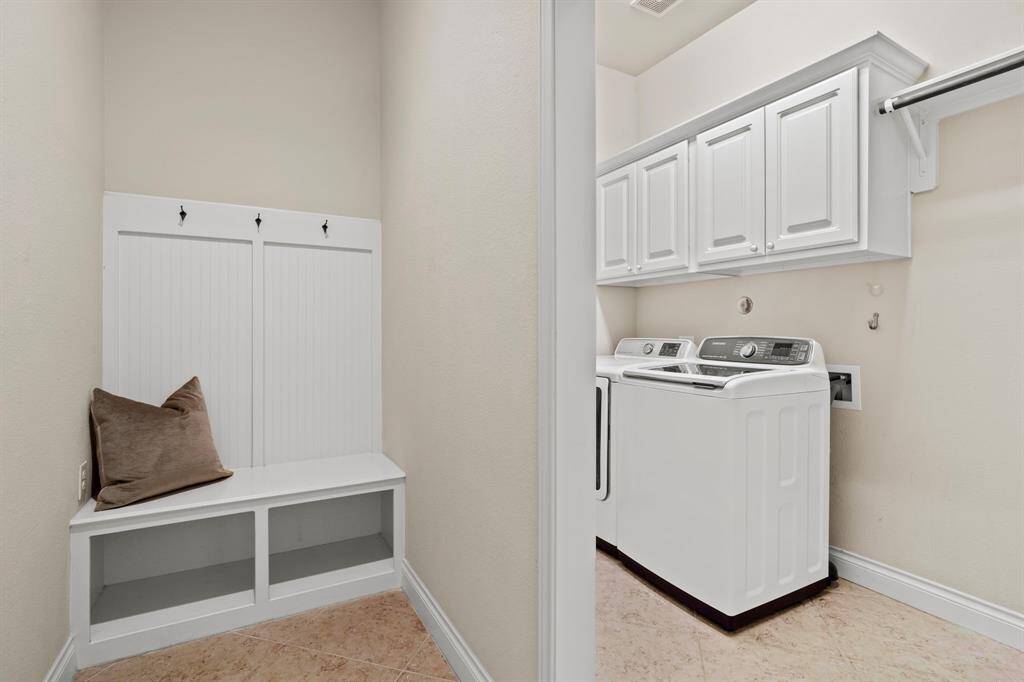 A built-in drop zone with storage and hooks welcomes you from the garage, leading into the utility room with upper cabinets, hanging bar, and plenty of space for laundry essentials.