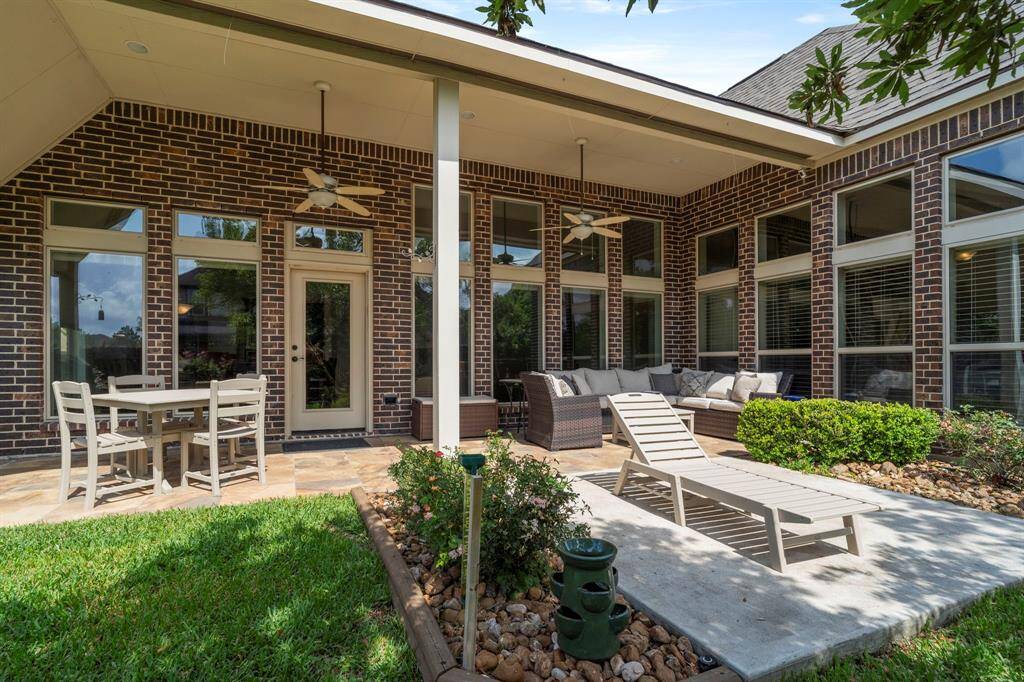 Enjoy outdoor living year-round on the spacious covered patio featuring ceiling fans, lush landscaping, and plenty of room for dining or lounging in the shade.