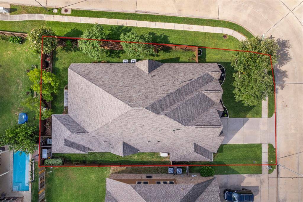 A top-down view reveals the home’s impressive roofline, lush green space, and mature trees along the perimeter.