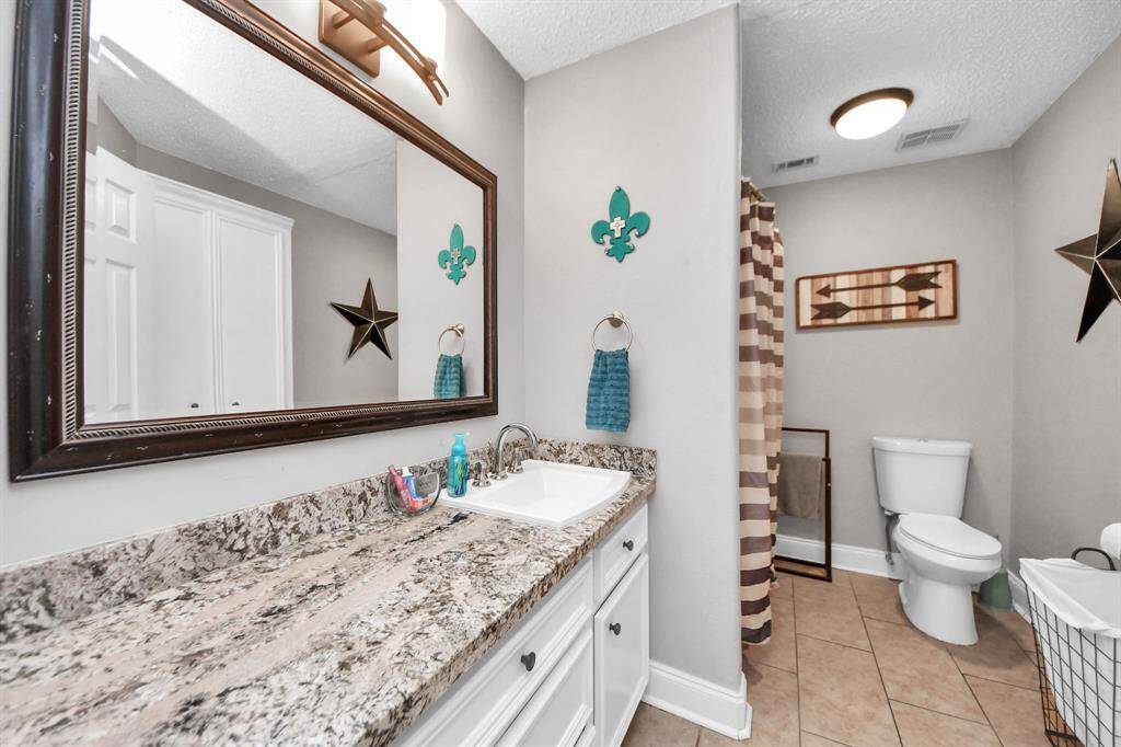 First secondary bathroom featuring granite countertops, a shower-tub combo, and built-in storage space for added convenience.