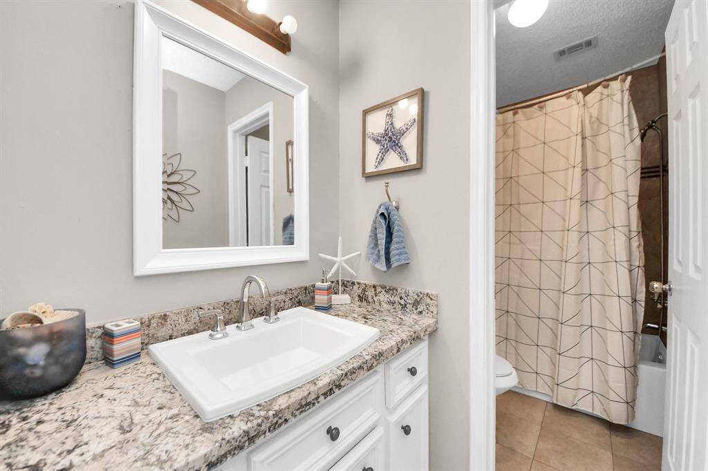 Second secondary bathroom with a tub-shower combo, granite countertops, and plenty of cabinet storage.