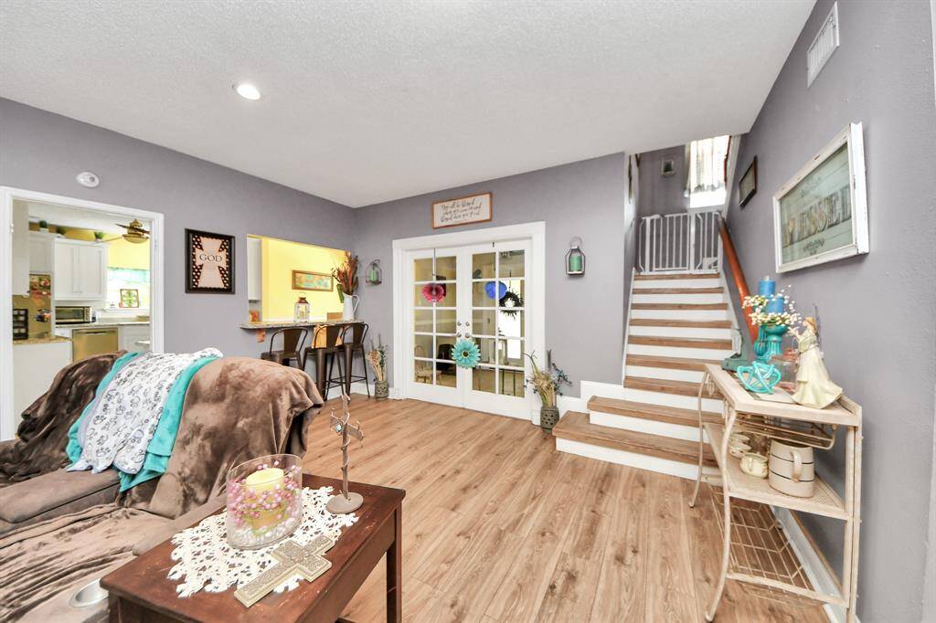 This inviting living area features warm wood flooring, a cozy seating arrangement, and a neutral color palette. It includes a staircase leading upstairs and a view into the kitchen, offering an open and welcoming layout.
