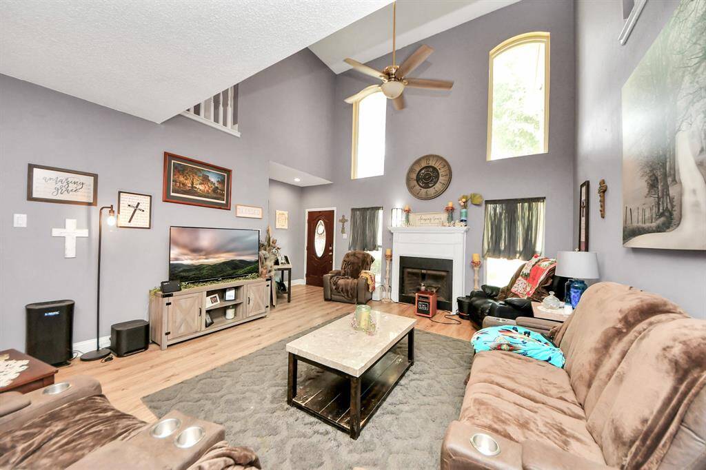 This inviting living room features high vaulted ceilings and large arched windows, allowing for abundant natural light. It also includes a cozy fireplace.