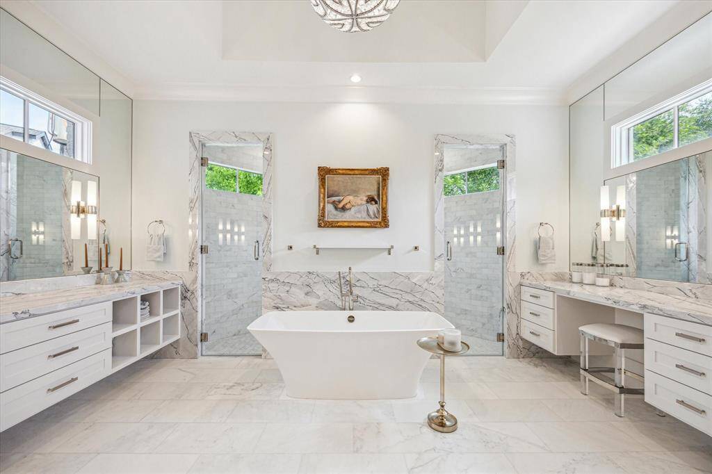 Primary bath with his and her marble topped vanities, heated floors, abundant natural light, tray ceiling, and elegant plumbing and lighting fixtures.  The over-sized shower through the glass doors is the epitome of luxury.