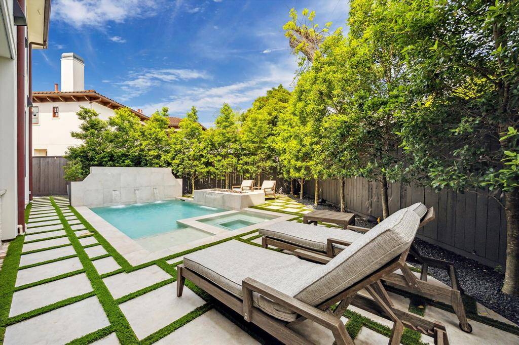 The mini- pebble finish pool with travertine coping has waterfall features, integrated hot tub, gas firepit.  Note the trees lining the cedar fence, as well as the easy maintenance provided by the stone and turf design.